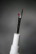 Sewing needle with white handle and red bead on a gray background