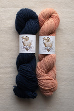 Load image into Gallery viewer, Two skeins of yarn, one navy and one peach, with labels on a beige background.