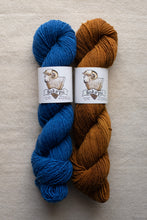Load image into Gallery viewer, Two skeins of blue and brown yarn with Soka&#39;pu labels on a beige background