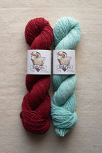 Load image into Gallery viewer, Two skeins of yarn, one red and one green, with labels on a beige background.