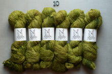 Load image into Gallery viewer, Six skeins of textured olive green yarn arranged in two rows on a light gray background, with white paper labels featuring a dog illustration and the brand name 'The Dog &amp; Yarn'. A small metal '10' scale is visible above the yarn.