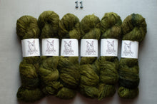 Load image into Gallery viewer, Six skeins of olive green yarn arranged in two rows on a light gray background, each wrapped with a white paper band featuring a black line drawing of a dog. A small metal number 11 is placed above the yarn.