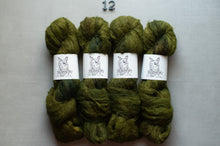 Load image into Gallery viewer, Four skeins of olive green yarn with white paper bands featuring a black line drawing of a dog, arranged side by side on a light gray background with the number 12 above them.