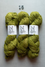 Load image into Gallery viewer, Three skeins of chunky, fuzzy yarn in a muted olive green color, arranged side-by-side on a light gray background with a small metal '15' weight marker above them. Each skein has a white paper label featuring a dog illustration and the brand name 'The Dog of War'.