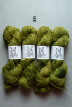 Load image into Gallery viewer, Four skeins of olive green yarn arranged in two rows on a light gray background, with a small metal '5' marker above them. Each skein has a white paper label featuring a llama illustration and the brand name 'Llamas of America'.