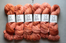 Load image into Gallery viewer, Six skeins of fluffy yarn in blended orange, peach, and coral shades, each wrapped with a white paper label featuring a black line drawing of a cat.