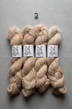 Load image into Gallery viewer, Four skeins of variegated yarn in soft peach, beige, and cream shades, arranged side by side on a gray background