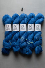 Load image into Gallery viewer, Five skeins of vibrant blue yarn arranged side-by-side on a neutral gray background, each wrapped with a white paper label