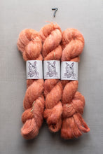 Load image into Gallery viewer, Three skeins of soft, fuzzy yarn in a peachy orange shade, each wrapped with a white paper label featuring a dog illustration and the text 'Pup Dye Co.', arranged on a gray background with a small black number 7 above them.
