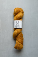 Load image into Gallery viewer, Mustard yellow skein of yarn with a label on a gray background