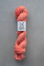 Load image into Gallery viewer, Peach-colored skein of yarn with a label on a gray background