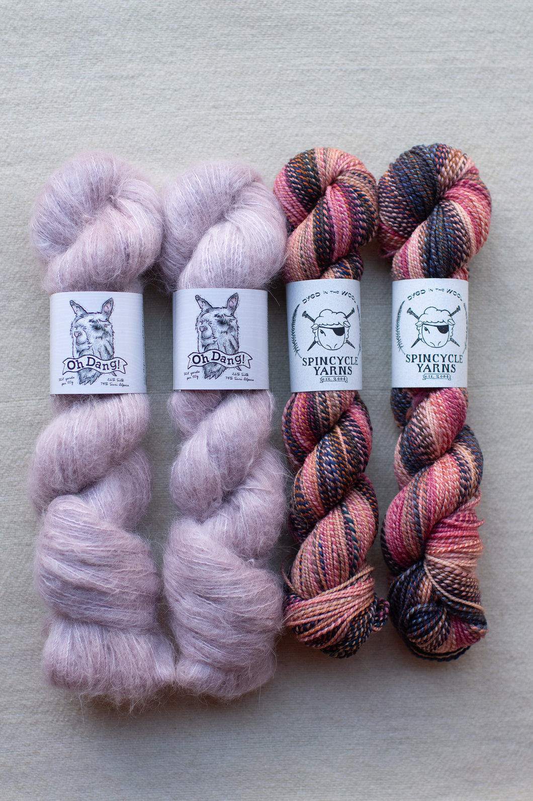 Four skeins of yarn in pink and multicolor on a gray background with labels.