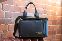 Load image into Gallery viewer, Black handbag with gold zipper on a brick wall background