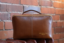 Load image into Gallery viewer, Brown leather pouch with 'Redesigned Project' branding against a brick wall background