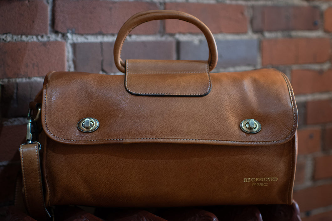 Brown leather bag with visible brand name against a brick wall background