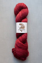 Load image into Gallery viewer, Red skein of yarn with a label on a gray background
