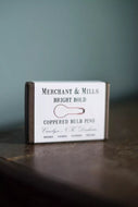 Box of Merchant & Mills copper bulb pins on a wooden surface with a dark background