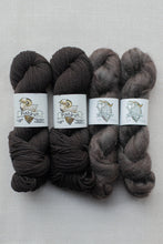 Load image into Gallery viewer, Four skeins of wool yarn arranged side by side on a light gray fabric background. The left two skeins are dark brown, and the right two are heathered gray-brown.