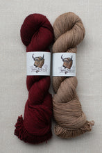 Load image into Gallery viewer, Two skeins of yarn side by side on a textured beige fabric background. The left skein is a deep burgundy red, and the right skein is a warm tan/beige.
