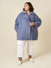 Load image into Gallery viewer, Woman wearing a blue coat and white pants on a beige background