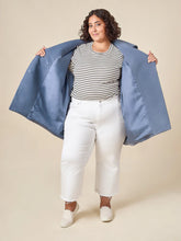 Load image into Gallery viewer, Woman wearing a blue jacket over a striped shirt and white pants on a beige background