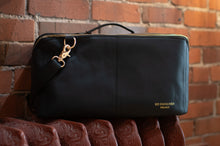 Load image into Gallery viewer, Black leather bag with gold zipper and 'Redesigned Project' branding against a brick wall.