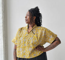 Load image into Gallery viewer, Woman wearing a yellow patterned blouse against a white wall