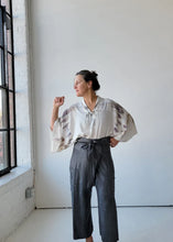 Load image into Gallery viewer, Woman wearing a white blouse with bell sleeves and dark pants in a minimalistic room.