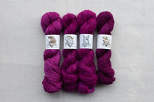 Load image into Gallery viewer, Four skeins of purple yarn with labels on a gray background