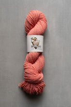 Load image into Gallery viewer, Peach-colored skein of yarn with a label on a gray background