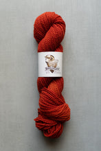 Load image into Gallery viewer, Red skein of yarn with a label on a gray background