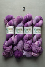 Load image into Gallery viewer, Four skeins of purple yarn with a label on a gray background
