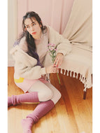 Person sitting on a wooden floor holding flowers, wearing a white coat and pink socks.