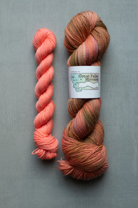 Two skeins of yarn, one pink and one multicolored, on a gray background with a label.