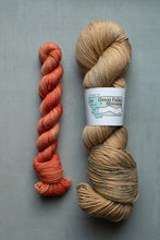 Load image into Gallery viewer, Two skeins of yarn, one red and one beige with a label, on a gray background