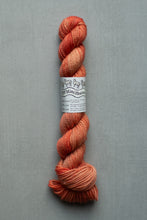 Load image into Gallery viewer, Skein of orange yarn with a label on a gray background