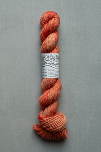 Skein of orange yarn with a label on a gray background