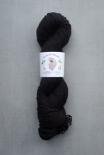 Load image into Gallery viewer, Black skein of yarn with a label on a gray background