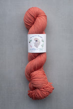 Load image into Gallery viewer, Coral skein of yarn with a label on a gray background