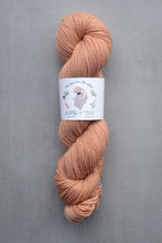 Load image into Gallery viewer, Peach-colored skein of yarn with a label on a gray background