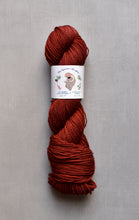 Load image into Gallery viewer, Red skein of yarn with a label on a gray background