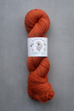 Load image into Gallery viewer, Orange skein of yarn with a label on a gray background