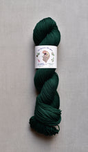 Load image into Gallery viewer, Dark green skein of yarn with a label on a gray background