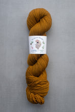 Load image into Gallery viewer, Mustard yellow skein of yarn with a label on a gray background