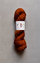 Load image into Gallery viewer, Ball of rust-colored yarn with a label on a gray background