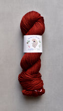 Load image into Gallery viewer, Red skein of yarn with a label on a gray background