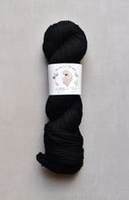 Load image into Gallery viewer, Black skein of yarn with a label on a gray background