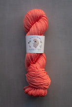 Load image into Gallery viewer, Peach-colored skein of yarn with a label on a gray background