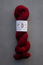 Load image into Gallery viewer, Red skein of yarn with a label on a gray background