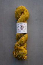 Load image into Gallery viewer, Mustard yellow skein of yarn with a label on a gray background